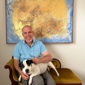 Artist Guy Trinquet with pet dog in front of gold and blue painting