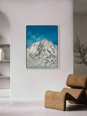 Framed mountain landscape art piece on a wall with a modern chair and shelves in the background.