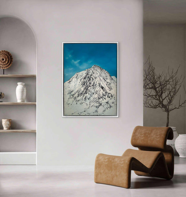 Framed mountain landscape art piece on a wall with a modern chair and shelves in the background.